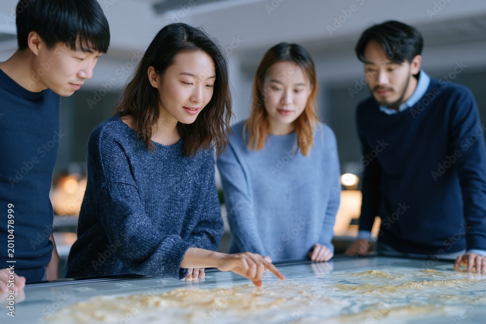 Fototapeta premium Collaboration and Innovation: Four individuals intently examine a complex plan spread before them, representing teamwork, strategy, and cutting-edge design. 