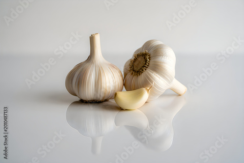 Organic garlic bulbs and a single clove on a reflective white kitchen surface