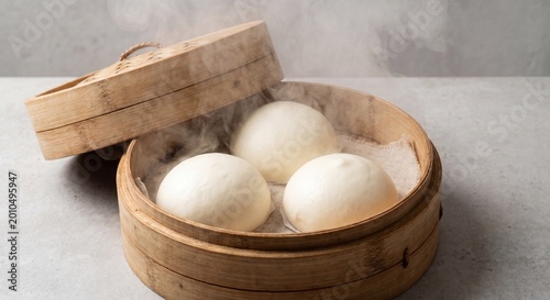 A professional product shot of three large Baozi nestled inside a traditional bamboo steamer basket (long). The tureen is partially open, with heavy steam swirling around the white, round buns. 