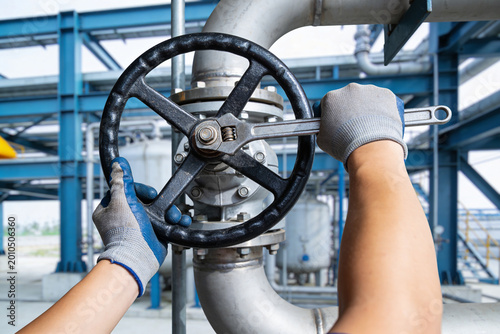 Industrial worker using a wrench to adjust a large valve wheel in a factory setting
