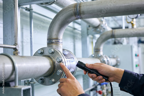 Foto Industrial worker inspects pipeline flange with flashlight, checking for leaks o