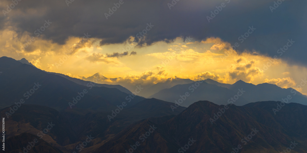 Obraz premium Dramatic Mountain Range Silhouette at Sunset with Golden Clouds