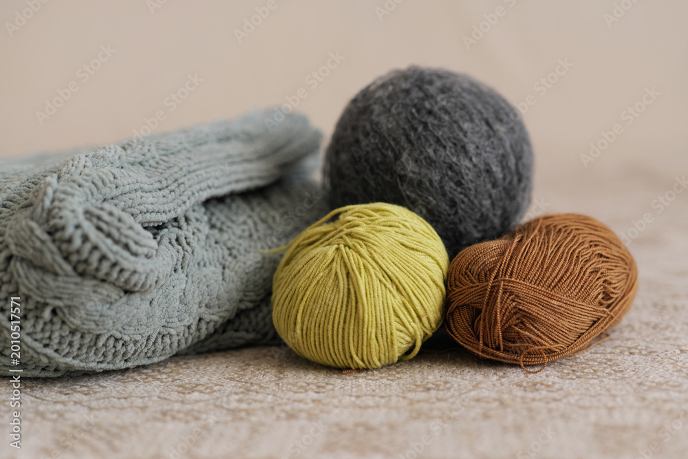 Fototapeta premium Knitting materials and three yarn balls are on a light-colored table. The yarn colors include green, brown, and gray, ready for use in a project