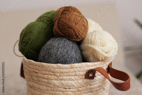 Yarn balls of different colors are placed together in a woven basket. The setting is bright and simple, ideal for knitting or crafting activities