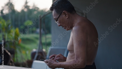 Fotografía Senior asian man concentrating on smartphone while standing outdoors in rural se