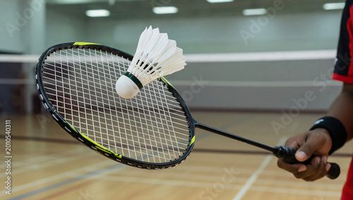 Badminton player hitting shuttlecock with racket in indoor sports court with wooden floor transparent background