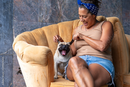 Bild auf Leinwand Woman playfully stretching pug dog's ears, sharing a joyful lifestyle moment