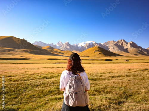 Fotografija Woman in hat and white T-shirt standing before mountains near Köl-Suu Lake in At-Bashy District, with vast alpine landscape