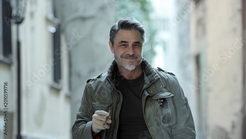 Portrait of stylish mature man confidently smiling in urban setting. Mid adult male smoking cigarette, looking confident and satisfied.