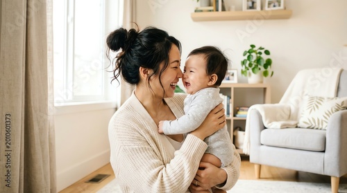 Asian mother playing with her adorable infant baby in bright home room.