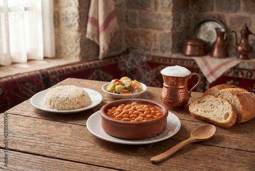 Traditional Turkish bean stew with rice pilaf, pickles, ayran and bread on rustic table