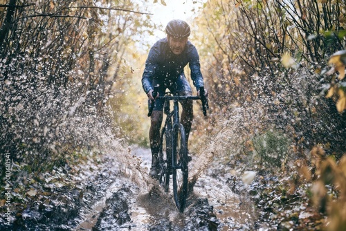 A cyclist navigating a muddy forest trail on a gravel bike, splashing water, dynamic action shot, autumn colors, highly detailed