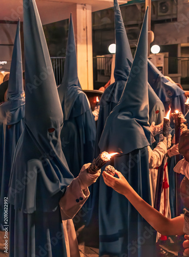 Foto penitentes de una hermandad dandole cera de los cirios a niños para hacer bolas