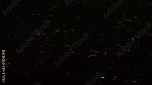 A close-up night view of the valley reveals a dense scatter of twinkling city lights, with faint outlines of buildings and curving roads glowing softly against the dark Mussoorie hills.