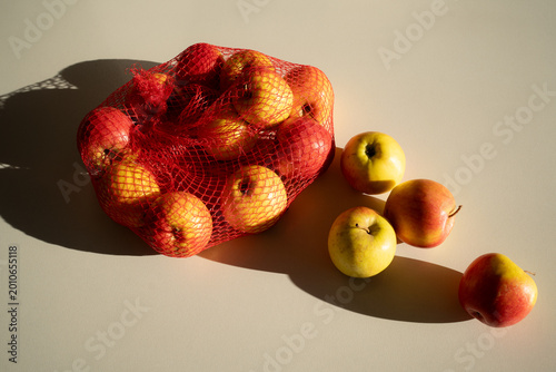 Fresh juicy yellow and red apples in a mesh bag on a white background, top view.