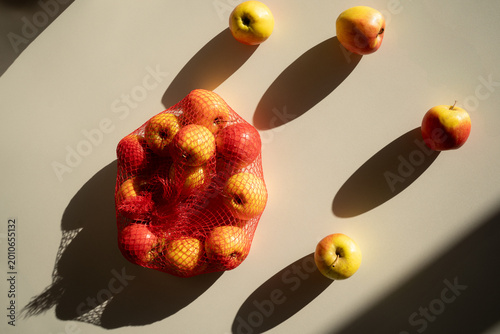 Fresh juicy yellow and red apples in a mesh bag on a white background, top view.