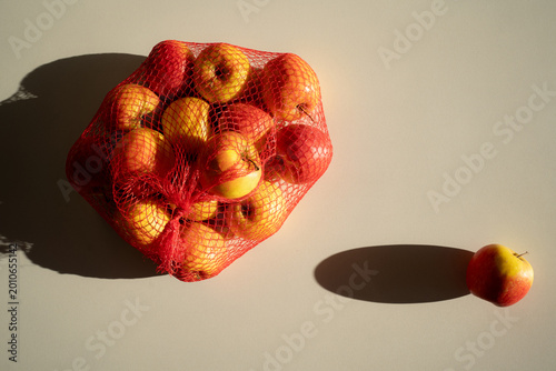 Fresh juicy yellow and red apples in a mesh bag on a white background, top view.