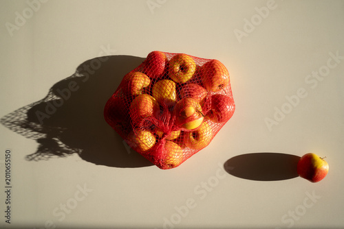 Fresh juicy yellow and red apples in a mesh bag on a white background, top view.