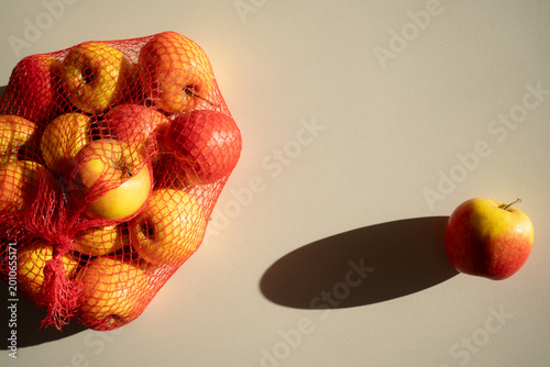 Fresh juicy yellow and red apples in a mesh bag on a white background, top view.