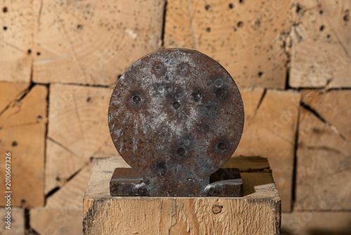 Close-up of a used round steel shooting target on a wooden block stand with fresh and old bullet marks after range practice