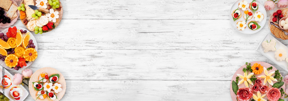 Obraz premium Summer garden party food double border. Variety of fun flower theme charcuterie items, fruit, crostini, finger sandwiches and dessert. Top down view on a white wood banner background.