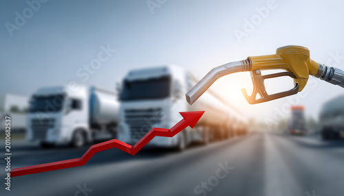 A gasoline nozzle with one fuel drop above blurry trucks and a red arrow graph indicating a rise in fuel prices.