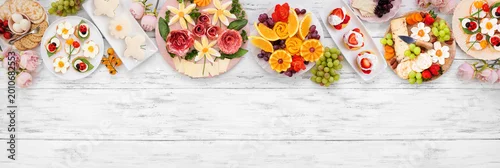 Panel kuchenny z motywem Summer garden party food top border. Assortment of fun flower theme charcuterie items, fruit, crostini, finger sandwiches and dessert. Overhead view on a white wood banner background.