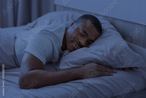 Cuadro en lienzo African american man sleeping at night in bedroom with blue light tone