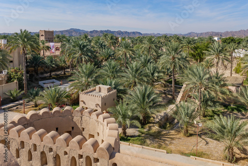 Fotografie View from Nizwa Fort in Oman overlooking sunlit clay walls and a lush palm grove