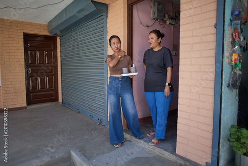 Two Women Engaging in Conversation Outside Their Home, Enjoying Refreshments on a Sunny Day, Showcasing Community and Social Interaction