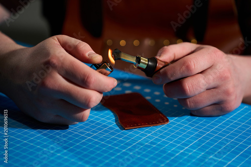 Photos Artisan using a lighter to heat an edge creaser over a blue cutting mat in a workshop