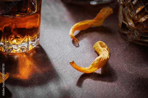 Closeup of whiskey glass reflection and orange peel garnish on textured dark tabletop, perfect for cocktail editorials, premium drink menus and luxury bar advertising