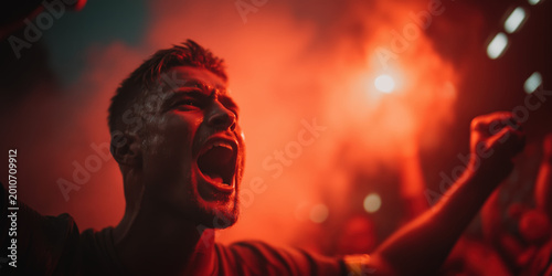 Male sports fan screaming with raised fist in red flare smoke atmosphere