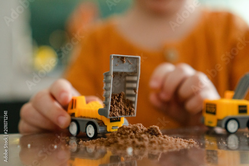 Foto Child hands play with two yellow toy dump trucks one dumping sand and dirt other empty