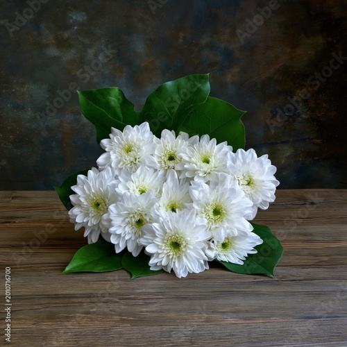 Bunch of White Flowers Placed on a Wooden Table With Green Leaves on a Neutra...