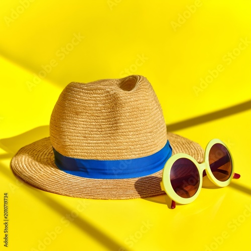 Summer Hat and Sunglasses on Bright Yellow Background in Warm Sunlight