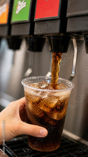 Carbonated soft drink poured from dispenser into plastic cup with ice. Fast food, self service and cold beverage concept.