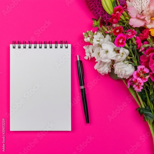 Bright Flowers and a Blank Notepad With a Pen on a Pink Background in a Creat...