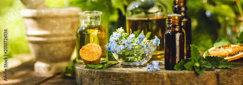 Banner. Mix of holistic flowers and herbs, salt, massage herb-infused essential oil in glass bottles. Aromatherapy, fragrance production. Herbal pure natural cosmetic ingredients on wooden background