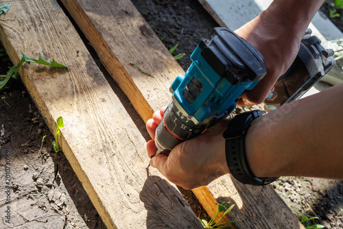Top view of a person using a cordless drill on old wooden planks on the ground