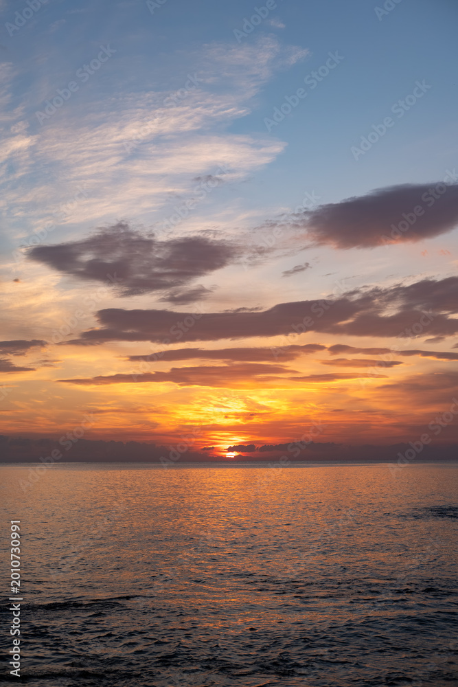 Fototapeta premium Vibrant sunset over calm ocean waters with colorful clouds reflecting on the surface, creating a serene coastal landscape at dusk