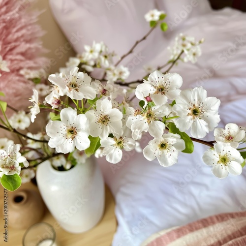 White Flower Branches in a Vase Next to a Bed With Soft Bedding and Decor