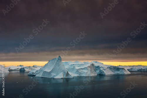 Bild auf Leinwand Glowing iceberg at sunset, bathed in golden light as the Arctic Ocean reflects a
