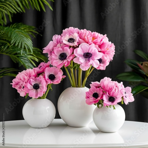 Bright Pink Flowers in White Vases on a Table With Green Plants and a Dark Ba...