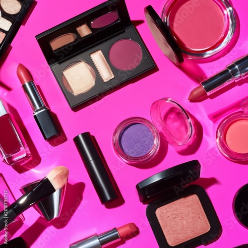 Many Makeup Products Arranged on a Bright Pink Surface for Showcasing and Sel...