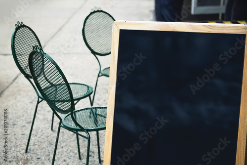 Green Metal Bistro Chairs and Blank Chalkboard Sign Outside Cafe