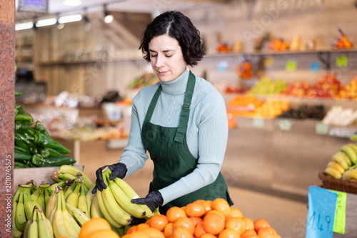 Foto While working in shop, employee forms display case, puts ripe imported banana in pile