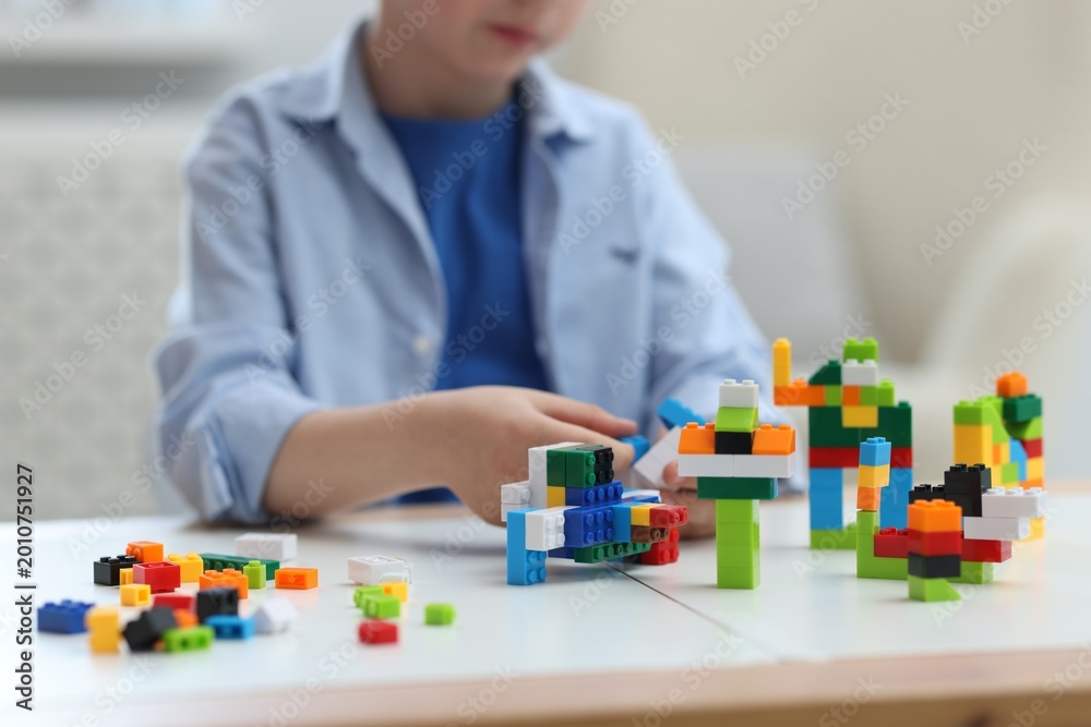 Fototapeta premium Construction toy. Little boy playing with building blocks at table indoors, closeup