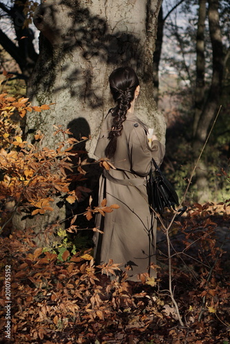 Small Girl with Braided Hair Wearing a Coat Standing with Back View in Autumn Forest