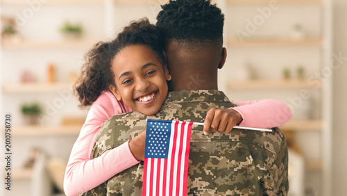Photos A child hugs a soldier from behind, holding an American flag